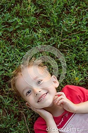 Little boy looking at camera lying on green grass Stock Photo