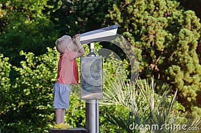 Little boy looking in telescope for tourists on observation deck. Green park background Stock Photo
