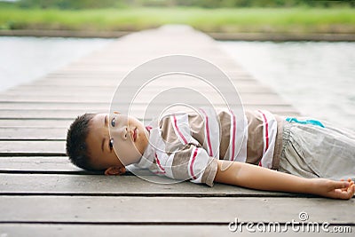 Little boy lying on wooden bridge at park. Stock Photo