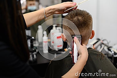 little boy in a mask, which is cut in the barbershop in the barbershop, fashionable and stylish haircut for a child. Stock Photo