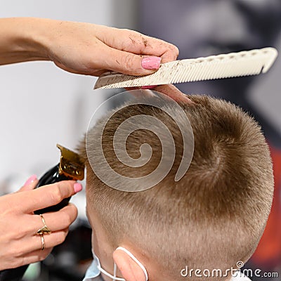 little boy in a mask, which is cut in the barbershop in the barbershop, fashionable and stylish haircut for a child. Stock Photo