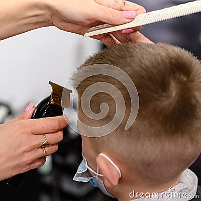 little boy in a mask, which is cut in the barbershop in the barbershop, fashionable and stylish haircut for a child. Stock Photo