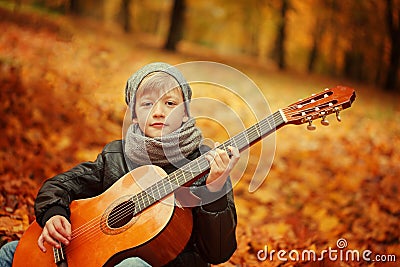 Little boy playing guitar on nature background, autumn day. Children's interest in music . Stock Photo