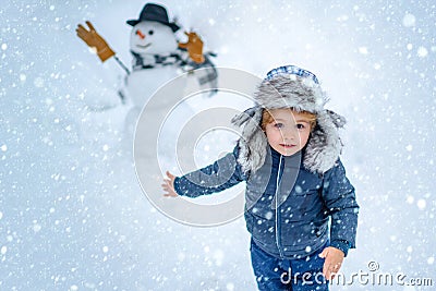 Little boy playing with snowman in winter park. Winter portrait of cute child in snow Garden. People in snow. Happy Stock Photo