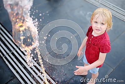 Little boy plays in the square between the water jets in the fountain at summer evening Stock Photo