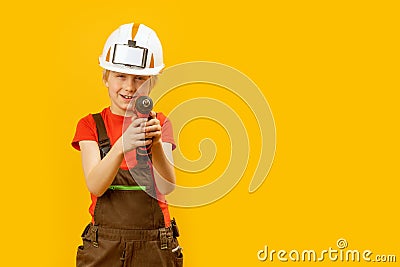 Little boy pretends to drill wall with drill against yellow isolated background. Boy teenager as builder worker. Copy space, Stock Photo