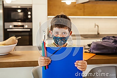 Little boy with a protective mask and school supplies at home ready for school. Horizontal Stock Photo