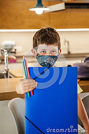 Little boy with a protective mask and school supplies at home ready for school. Vertical Stock Photo
