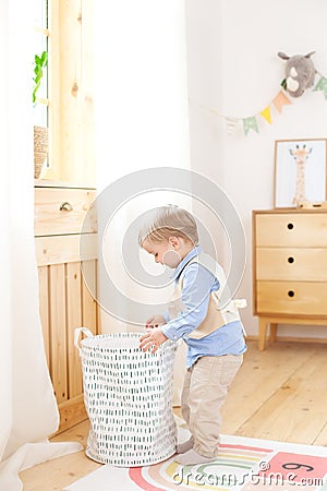 A little boy puts toys in a Scandinavian basket for a children`s room. Eco-friendly decor child`s room. Portrait of a boy playing Stock Photo