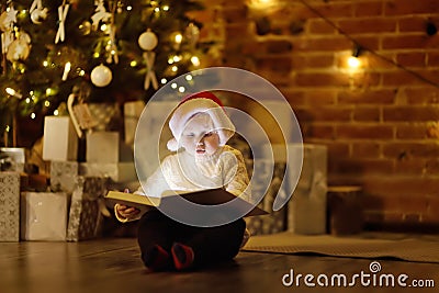 Little boy reading a magic book in decorated cozy living room. Portrait of happy kid on Christmas eve Stock Photo