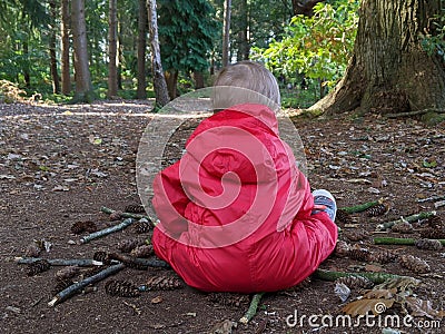 Little boy in a red waterproof sits in a mandala on the floor in the woods no blur Stock Photo