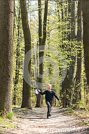 Little boy running hopping along the road in the forest enjoying warm sunny spring weather, holding his hat off in his hand Stock Photo