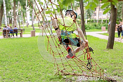 Little boy in safety equipment climbing on rope wall at adventure park. Children summer sport extreme outdoor activity. Back view Stock Photo