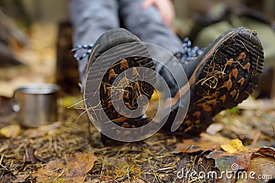 Little boy scout during hiking in autumn forest. Child is resting on large fallen tree and drinking hot tea. Legs close-up Stock Photo