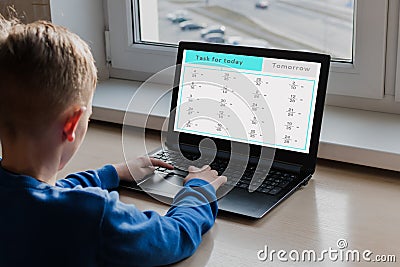 A little boy sits at a computer near the window Stock Photo