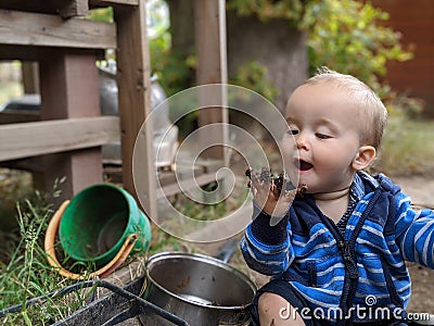 Little boy sitting on the ground looking at his muddy hand Stock Photo