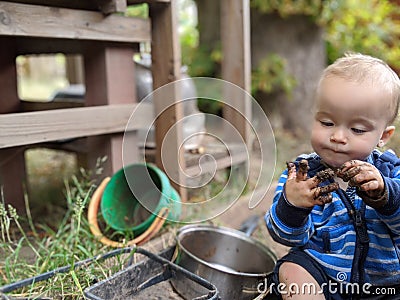 Little boy sitting on the ground looking at and picking his muddy hand Stock Photo