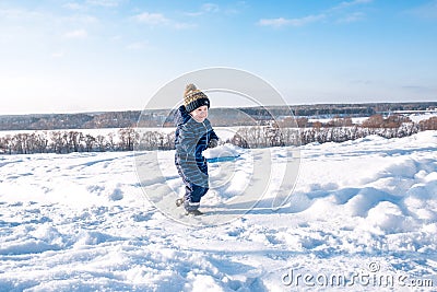 Little boy with a snow shovel in winter in the park. Happy carrying snow on a shovel in casual clothes. Stock Photo