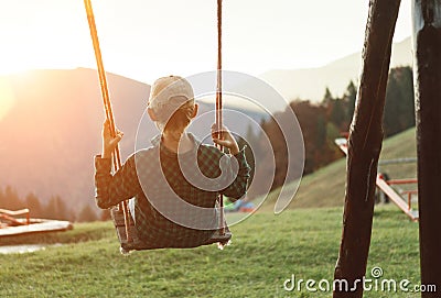 Little Boy swinging on the mountain kids park playground in the evening sunset rays. Careless childhood concept image Stock Photo