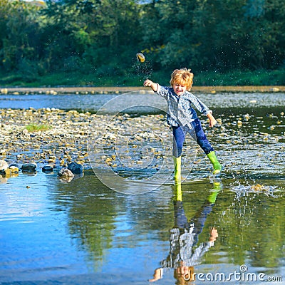 Little boy throw stones at the Stony river. Beautiful kids girl throws a rock at the river. Skipping Rocks. Boy Stock Photo