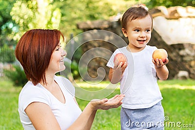 Little boy with two peaches and his mom on the picnic in the park. Son is holding fruits while mother is asking to share one. Both Stock Photo