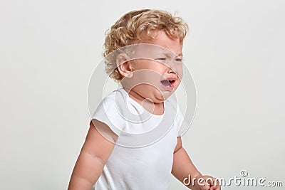 Little boy wearing t shirt cries, being in bad mood, looking away, posing isolated over white background, finding close person, Stock Photo