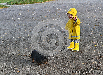 Little boy wearing yellow rain coat walking with his dog Stock Photo