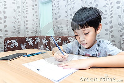 Little boy writing homework on wooden table at home. Kid learing and writing alphabet looking very happy Stock Photo