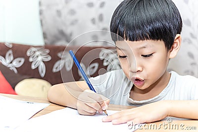 Little boy writing homework on wooden table at home. Kid learing and writing alphabet looking very happy Stock Photo