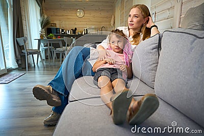 Little braided girl leaning on mother& x27;s laps sitting on sofa Stock Photo