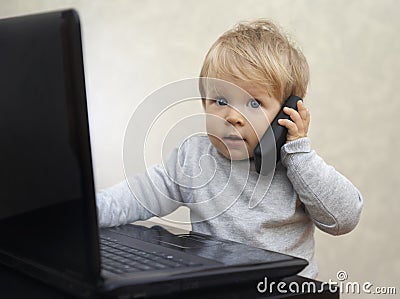 Little businessman sitting at the computer with a toy cell phone Stock Photo