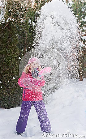 Little Caucasian blond girls in red jacket is playing with snow on fir-tree blur background Stock Photo