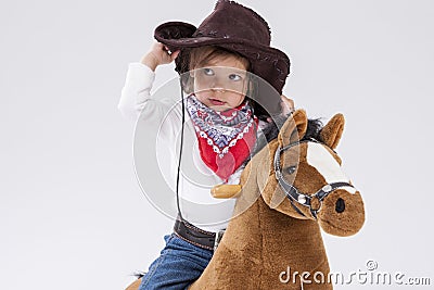Little Caucasian Girl in Cowgirl Clothing Posing On Symbolic Horse Against White. Holding Her Stetson Stock Photo
