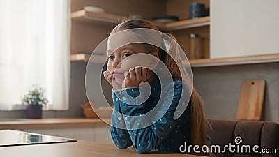 Little Caucasian sad upset child girl sitting at home kitchen alone offended kid schoolgirl feeling disappoint bullied Stock Photo