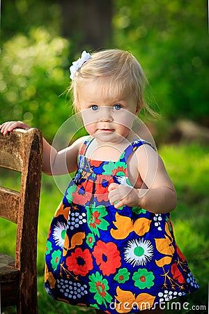 Little caucasian toddler stands using chair for support outside Stock Photo