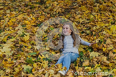 Little charming girl child throws up fallen yellow maple leaves in autumn park Stock Photo