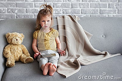 Little charming girl sits on a gray sofa. Stock Photo