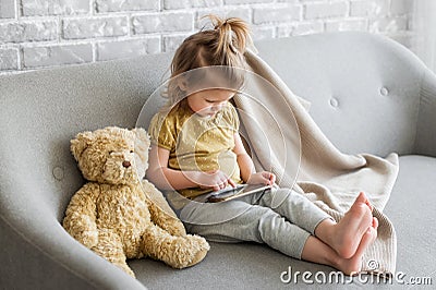 Little charming girl sits on a gray sofa. Stock Photo