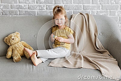 Little charming girl sits on a gray sofa. Stock Photo