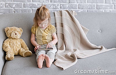 Little charming girl sits on a gray sofa. Stock Photo