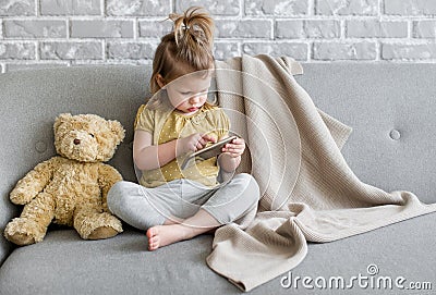 Little charming girl sits on a gray sofa. Stock Photo