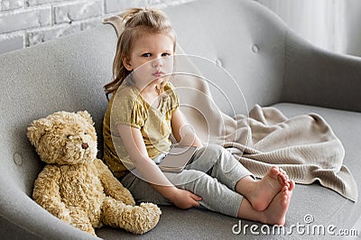 Little charming girl sits on a gray sofa. Stock Photo