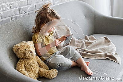 Little charming girl sits on a gray sofa. Stock Photo