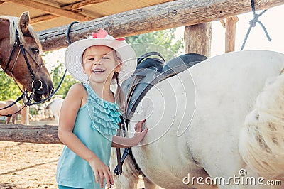 Little cheerful girl and the horse. Girl in a hat Stock Photo