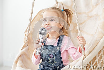 A little cheerful girl sings a song into the microphone. The con Stock Photo