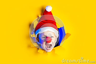 Little cheerful Santa in hat smiles, getting out of the ragged yellow background lit by neon light Stock Photo