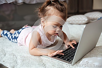 Little child girl lies on bed indoors using laptop computer Stock Photo