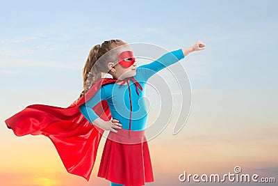 Little child girl plays superhero. Child on the background of sunset sky. Stock Photo