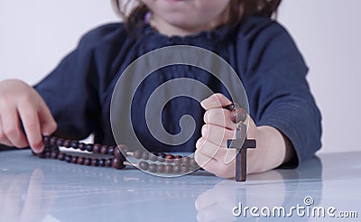 Little child girl praying and holding a wooden rosary as symbol of belief and faith in Jesus Christ and eternal life Stock Photo