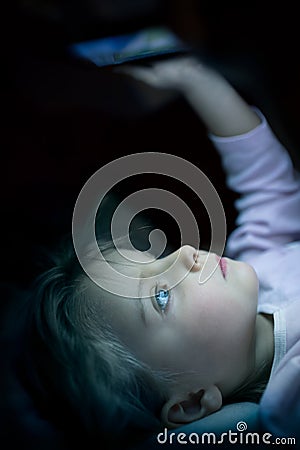 Little child girl using tablet technology in bed by night at home. Serious or toughtful kid daughter in bedroom watching Stock Photo